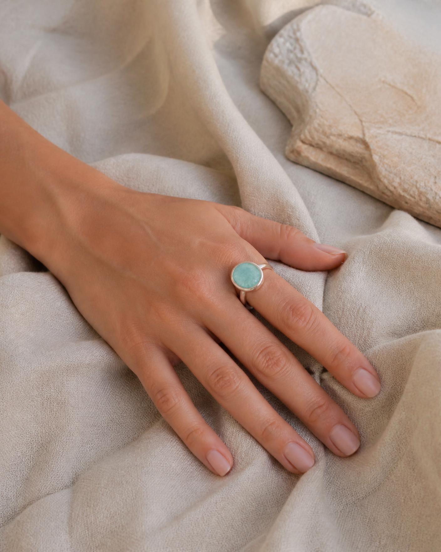 Hand wearing the Tidal Amazonite Ring resting on natural linen in soft coastal daylight.