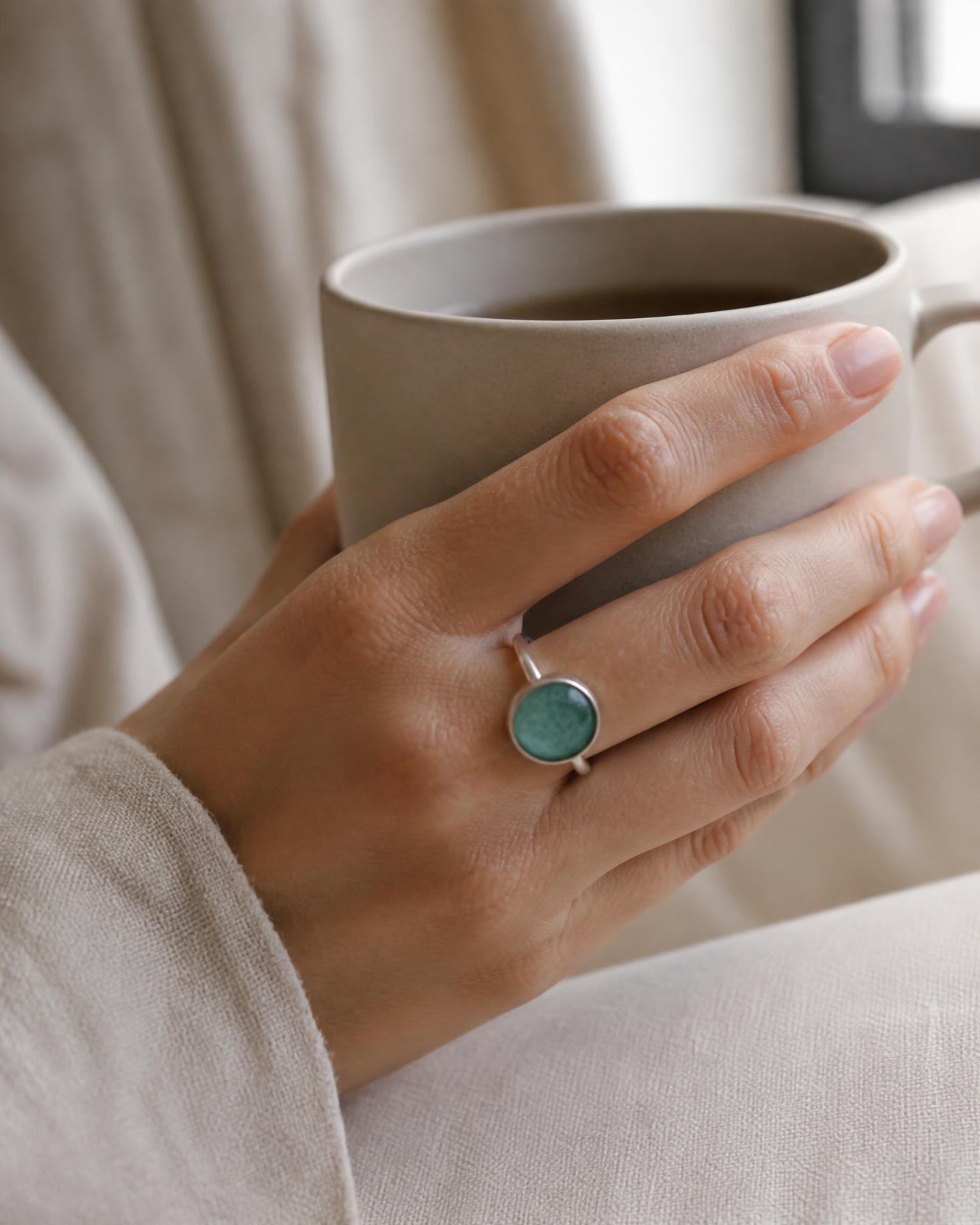 Hand wearing the Tidal Amazonite Ring while holding a ceramic coffee cup in morning light.